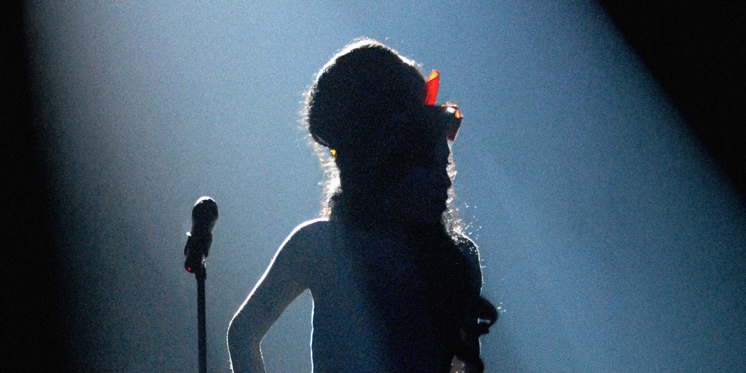 Amy Winehouse silhouette on stage under dramatic lighting with her signature beehive hairstyle