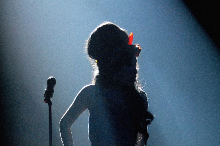 Amy Winehouse silhouette on stage under dramatic lighting with her signature beehive hairstyle