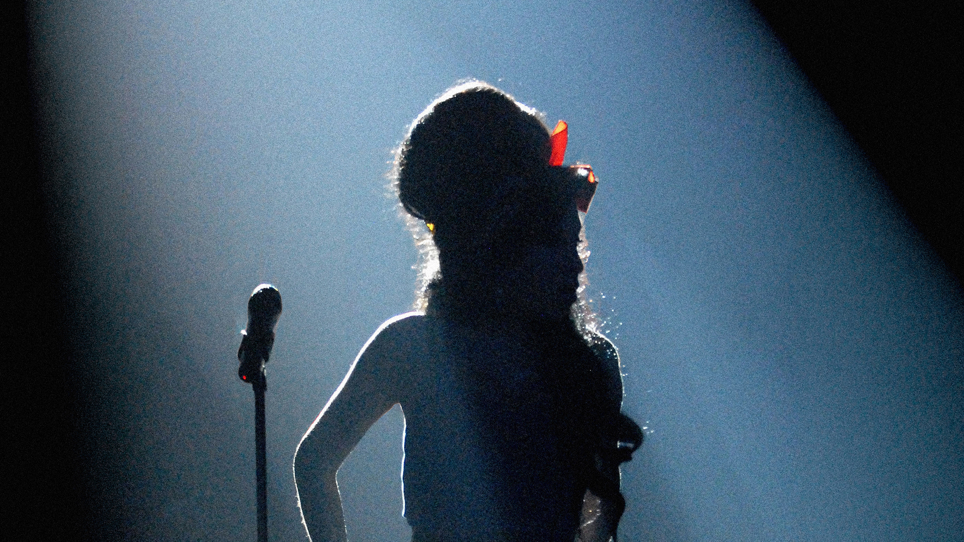 Amy Winehouse silhouette on stage under dramatic lighting with her signature beehive hairstyle