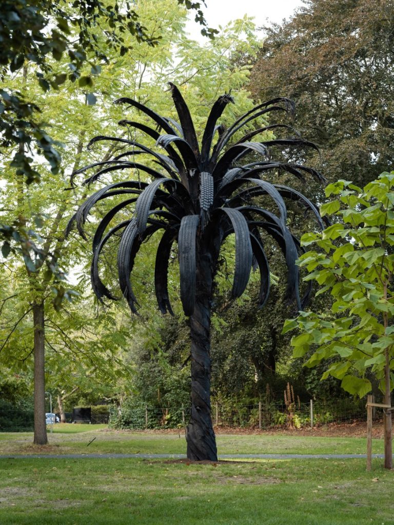 Douglas White's Black Palm sculpture resembling a large dark palm tree with sweeping black fronds, installed among trees at Frieze Sculpture 2026.
