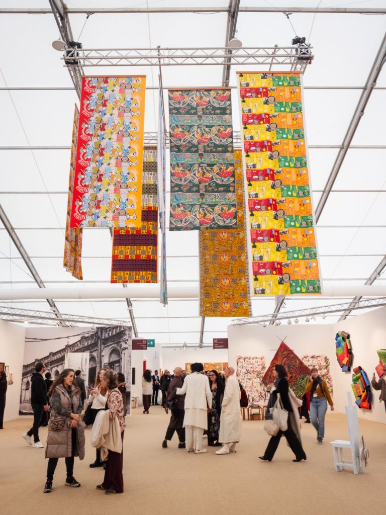 Colourful patterned textile artworks suspended above visitors at the Echoes in the Present exhibition during Frieze London 2025.