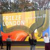 Visitors stand before the colourful Frieze London entrance sign beneath autumn trees in Regent’s Park.