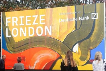 Visitors stand before the colourful Frieze London entrance sign beneath autumn trees in Regent’s Park.