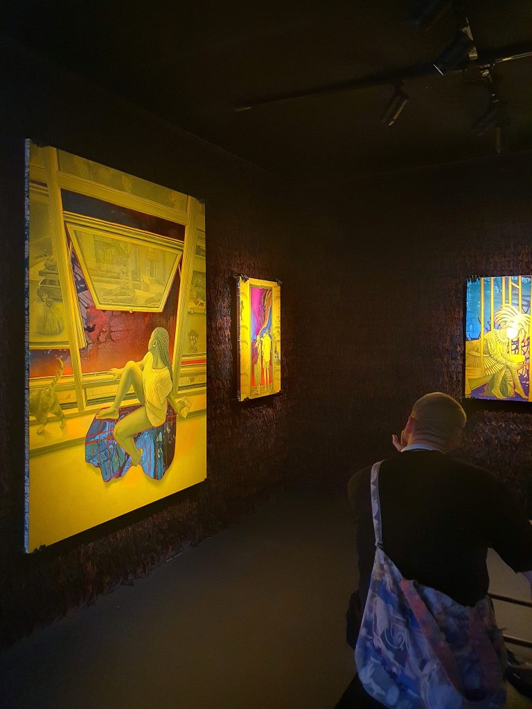 A visitor views Ken Nwadiogbu’s yellow figurative paintings against dark, fringed textile walls.