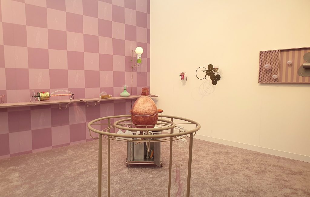 Steph Huang installation with pink checked walls, repurposed food tins and an oversized egg-shaped sculpture on a metal stand.