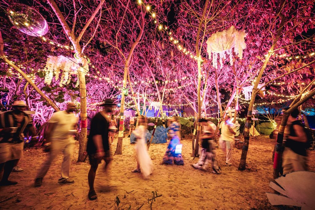 Festivalgoers walking through a tropical beach setting illuminated by pink lights and hanging decorations at SXM Festival 2026