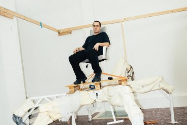 Artist Theo Triantafyllidis seated on his large spider-like Feral Metaverse sculpture inside his Athens studio.